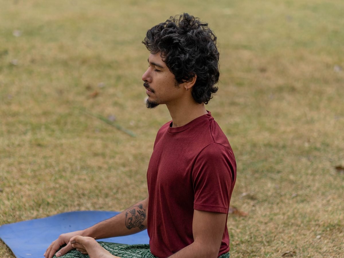 Man meditating in a seated yoga pose on a mat outdoors